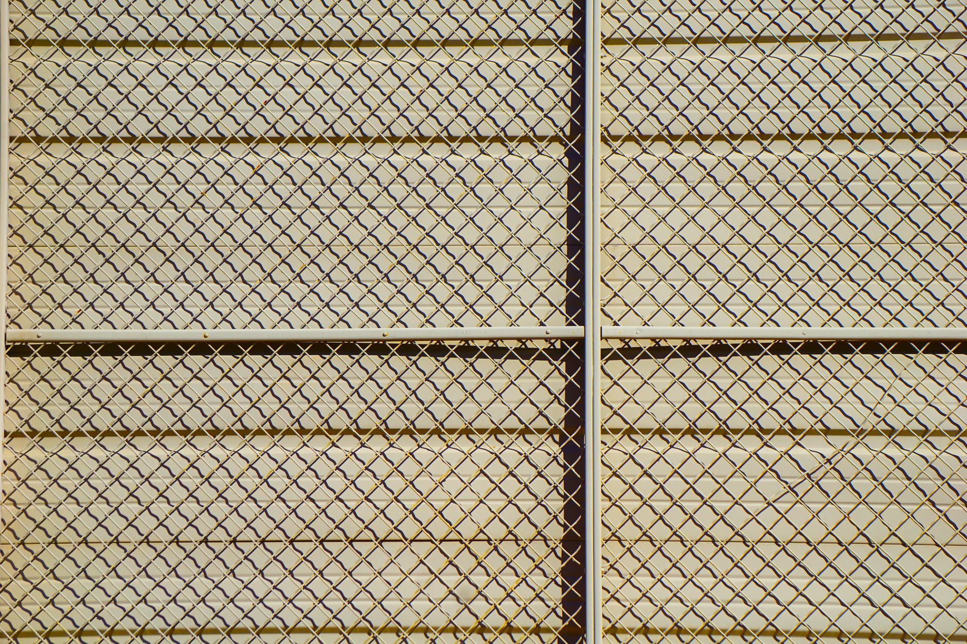 Textured grid pattern of a chain-link fence casting shadows, showing how fence style changes the finished look and price